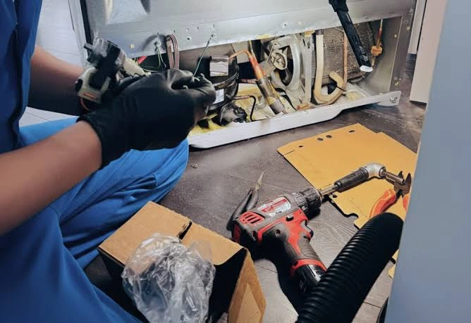 Gloved technician servicing refrigerator components with repair tools nearby