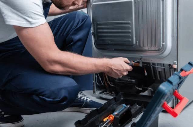 Technician repairing refrigerator components behind its rear panel